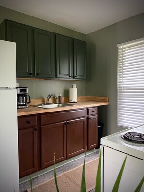 Una cocina con armarios de madera, un refrigerador blanco, una cafetera y una ventana con persianas.