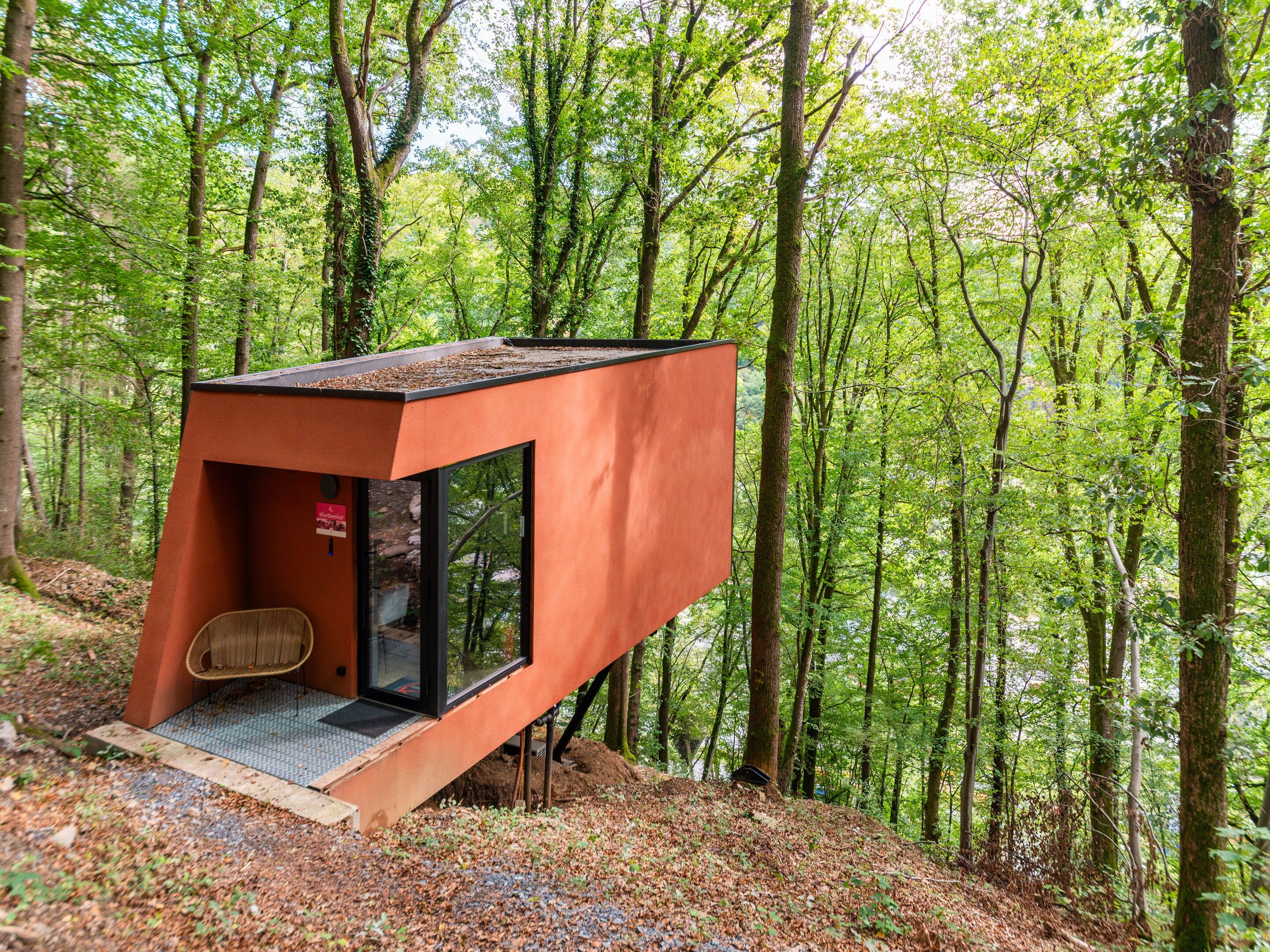 A modern treehouse with a glass entrance and a small seating area.
