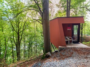 Ein kleines, rotes Gebäude mit einer Bank, umgeben von bewaldetem Gebiet.