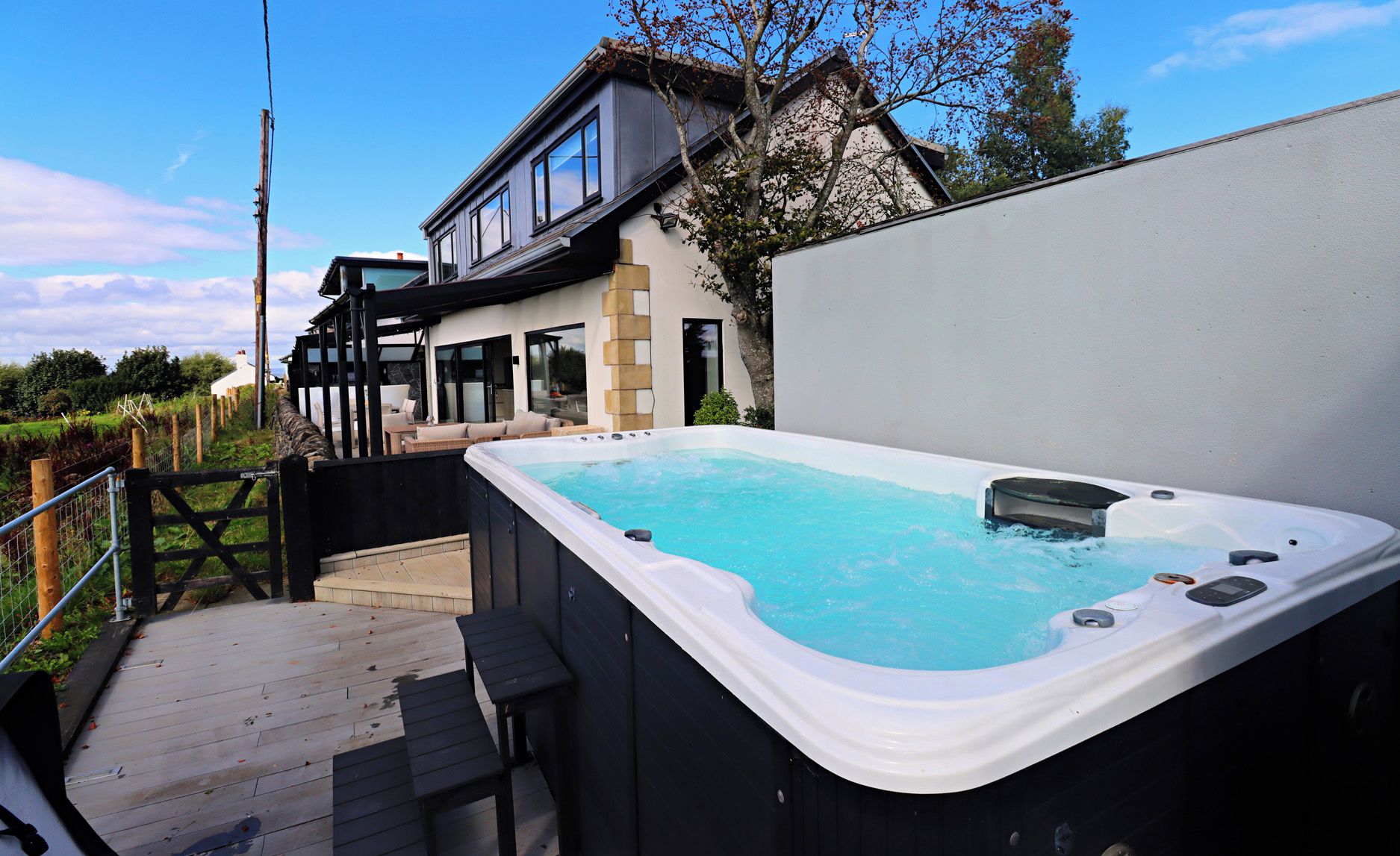 Un bain à remous dans un jardin, avec une terrasse en bois et une maison en arrière-plan.