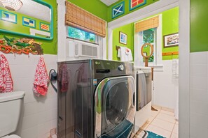 A compact laundry room with a front-loading washer and dryer, a toilet, and a window with blinds. - Historic Shadow Point - Private Waterfront Estate & Gardens on 2.5 Acres! (Key Largo)