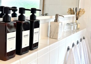 A bathroom with three bottles of body wash and conditioner, a marble soap dish, and towels hanging on a rack.