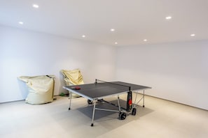 Uma mesa de tênis de mesa em um ambiente com paredes brancas e piso revestido de azulejos.