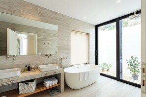 Ein modernes Badezimmer mit einem großen Spiegel, zwei Waschbecken, einer Badewanne und einem Fenster mit Blick auf Grünflächen.
