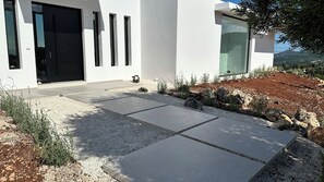 Um edifício moderno com porta preta, caminho de cascalho e área de jardim com pedras.