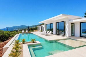 Ein moderner Poolbereich mit klarem, blauen Wasser, umgeben von Liegestühlen und einem Gebäude mit großen Fenstern.