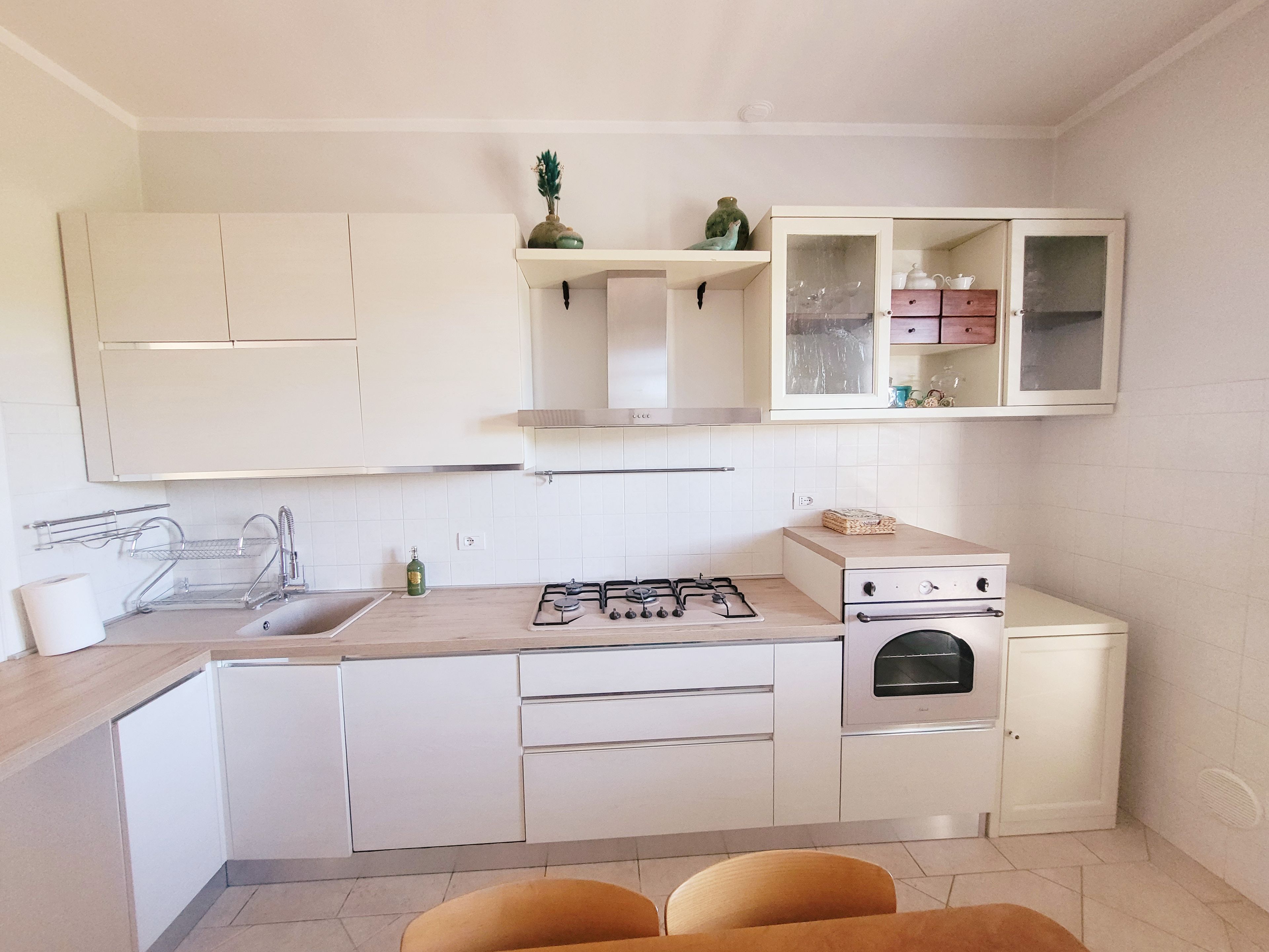 A modern kitchen with white cabinets, a gas stove, a built-in oven, and a small dining area with two chairs.
