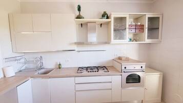 A modern kitchen with white cabinets, a gas stove, a built-in oven, and a small dining area with two chairs.