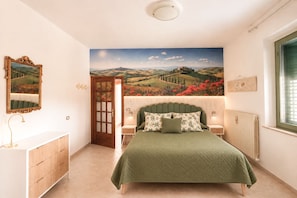 A bedroom with a bed, a nightstand, a dresser, a door, and a wall mural. - Lupin House with a large, air-conditioned veranda and Wi-Fi (Toscana)