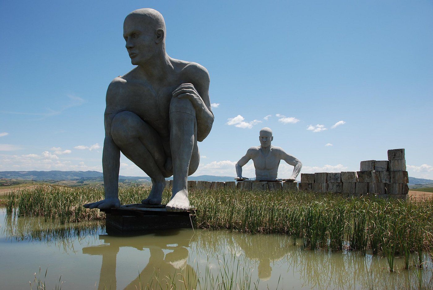 A sculpture of a seated man in a natural landscape with a clear sky.