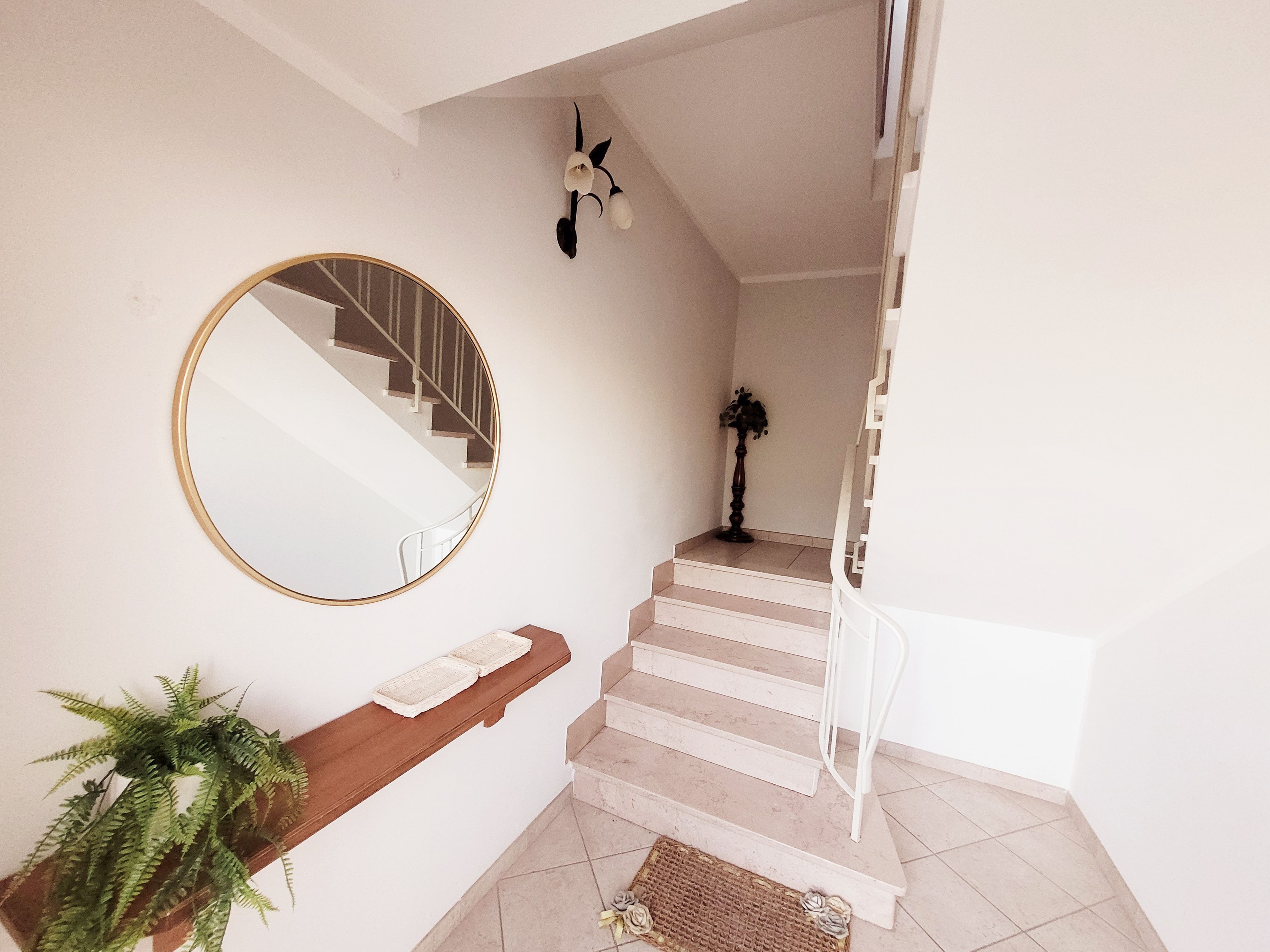 A staircase with a round mirror, a potted plant, and a small table with a book.