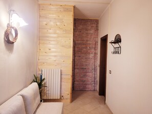 A hallway with a wooden panel wall, a radiator, a white sofa, a potted plant, and a brick wall in the background. - Lupin House with a large, air-conditioned veranda and Wi-Fi (Toscana)