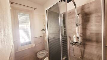 Un bagno moderno con doccia vetrata, un water e una finestra con persiane.