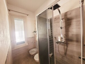 Un bagno moderno con doccia vetrata, un water e una finestra con persiane.