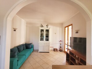 A living room with a green sofa, a white cabinet, and a TV stand. - Lupin House with a large, air-conditioned veranda and Wi-Fi (Toscana)