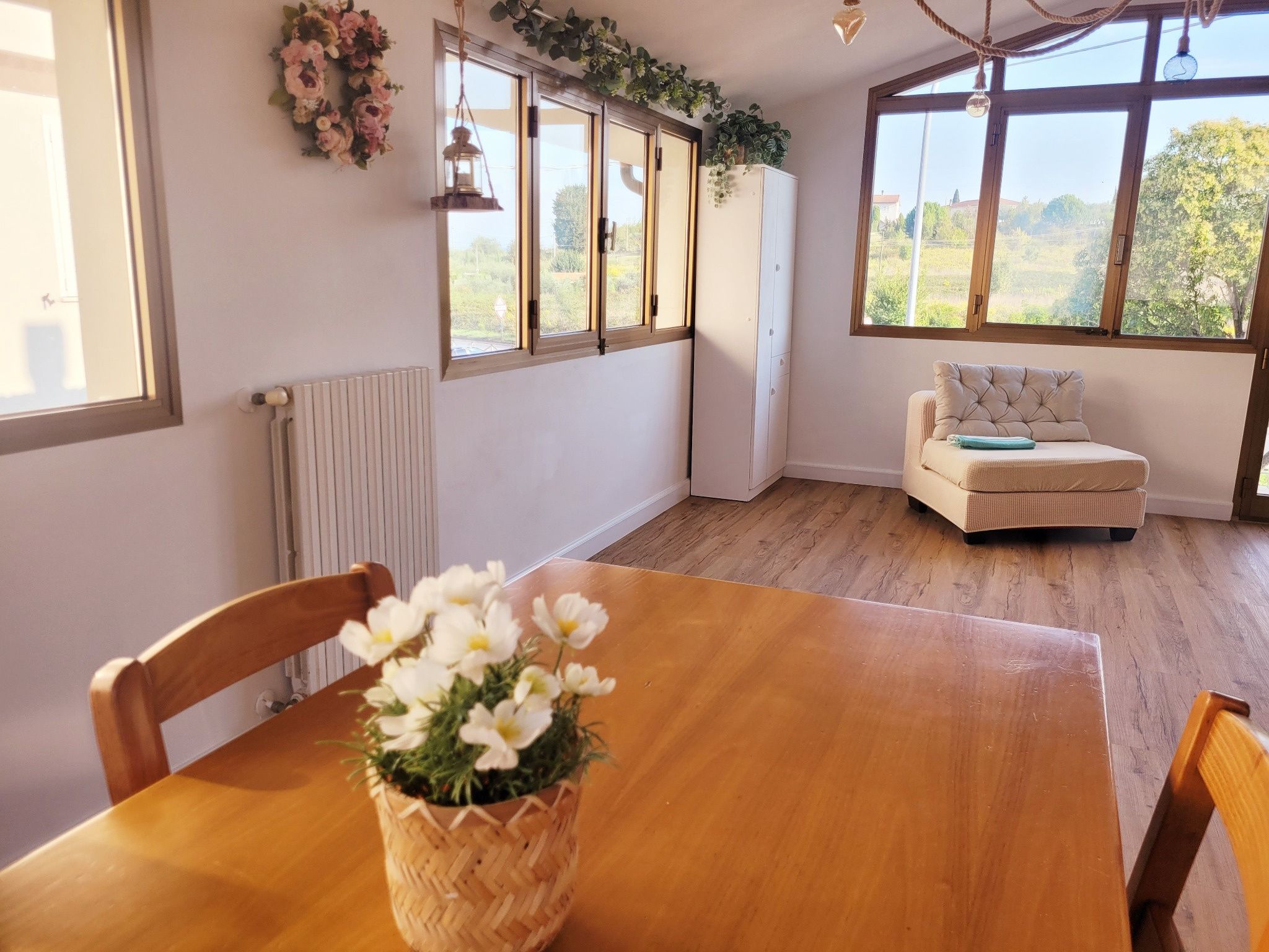 Une pièce avec une table en bois, des chaises, un canapé et de grandes fenêtres donnant sur un paysage verdoyant.