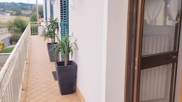 En balkong med kakelgolv, krukväxter, en dörr med ett glasparti och ett vitt räcke.