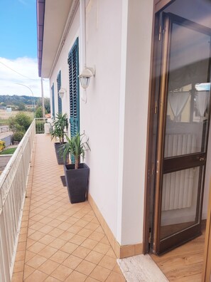 A balcony with tiled flooring, potted plants, a door with a glass panel, and a white railing. - Lupin House with a large, air-conditioned veranda and Wi-Fi (Toscana)