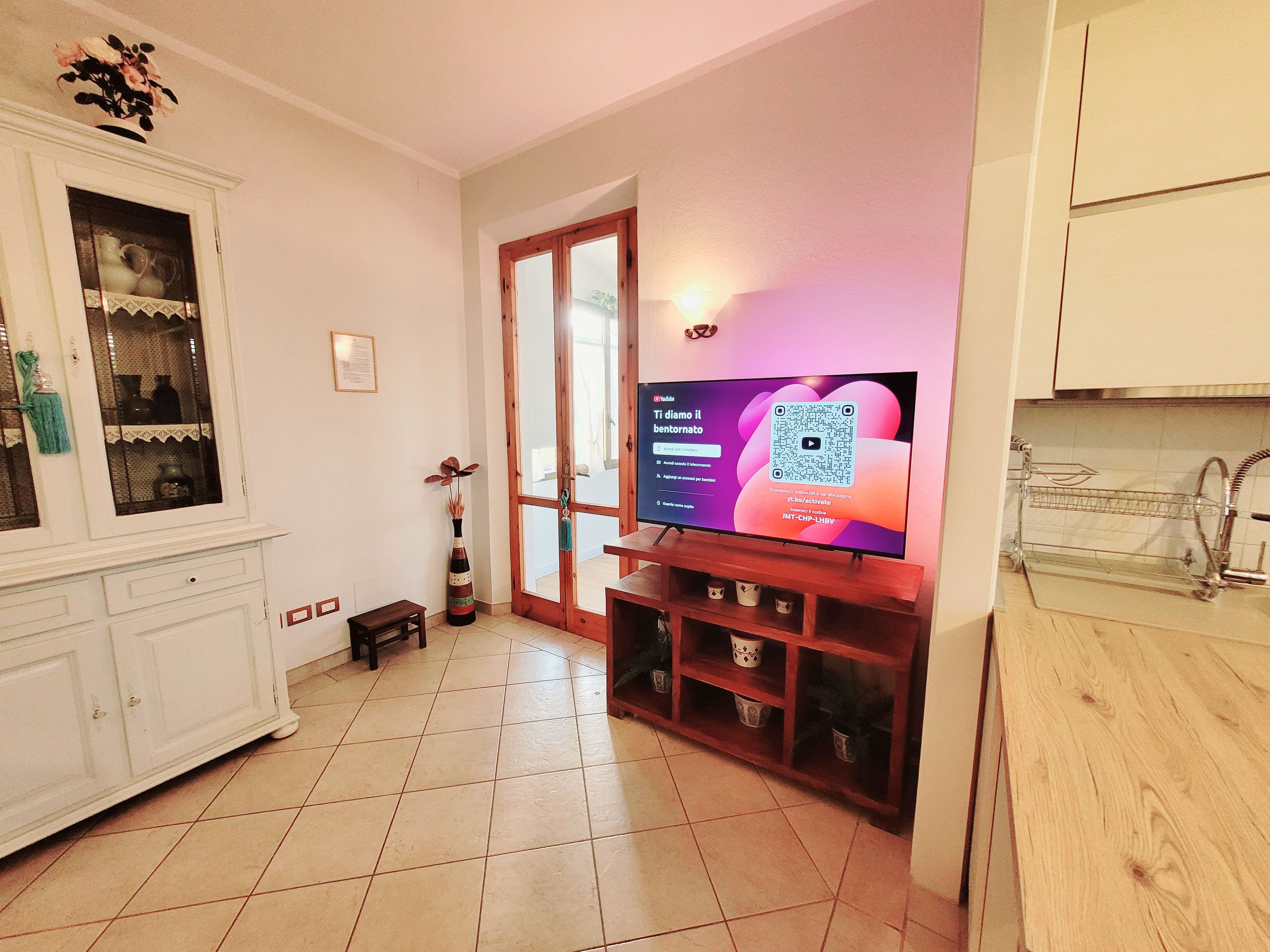 A living room with a television on a wooden stand, a cabinet with glass doors, and a tiled floor.