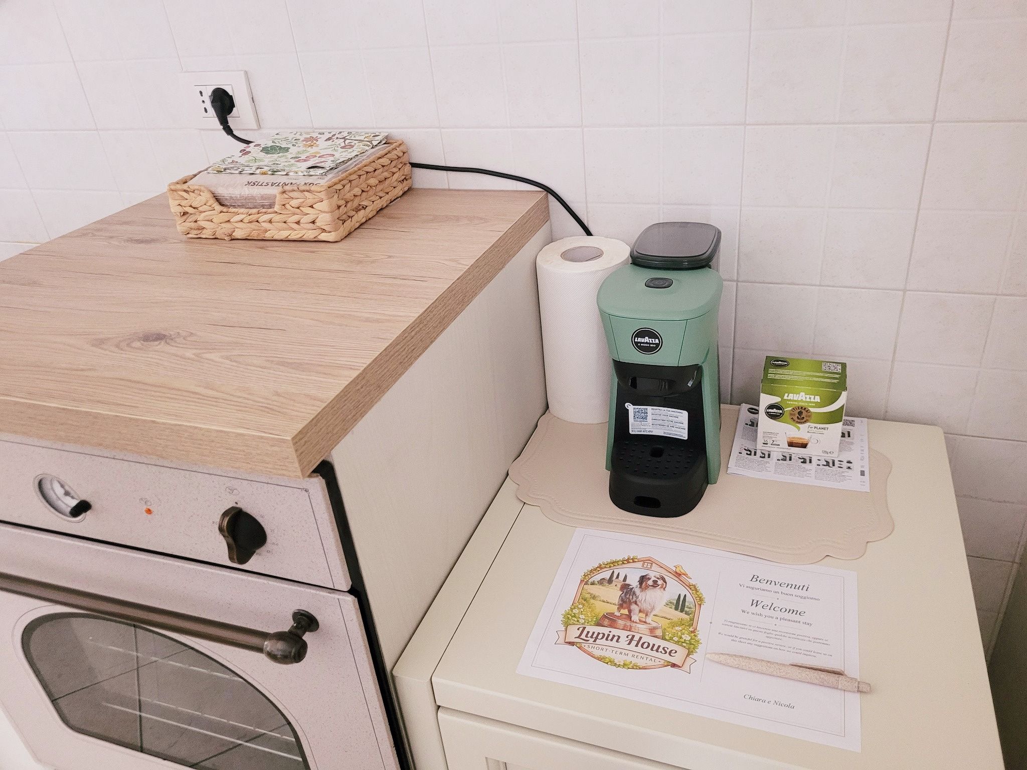 A kitchenette with a coffee maker, a roll of paper towels, a basket, and a welcome card.