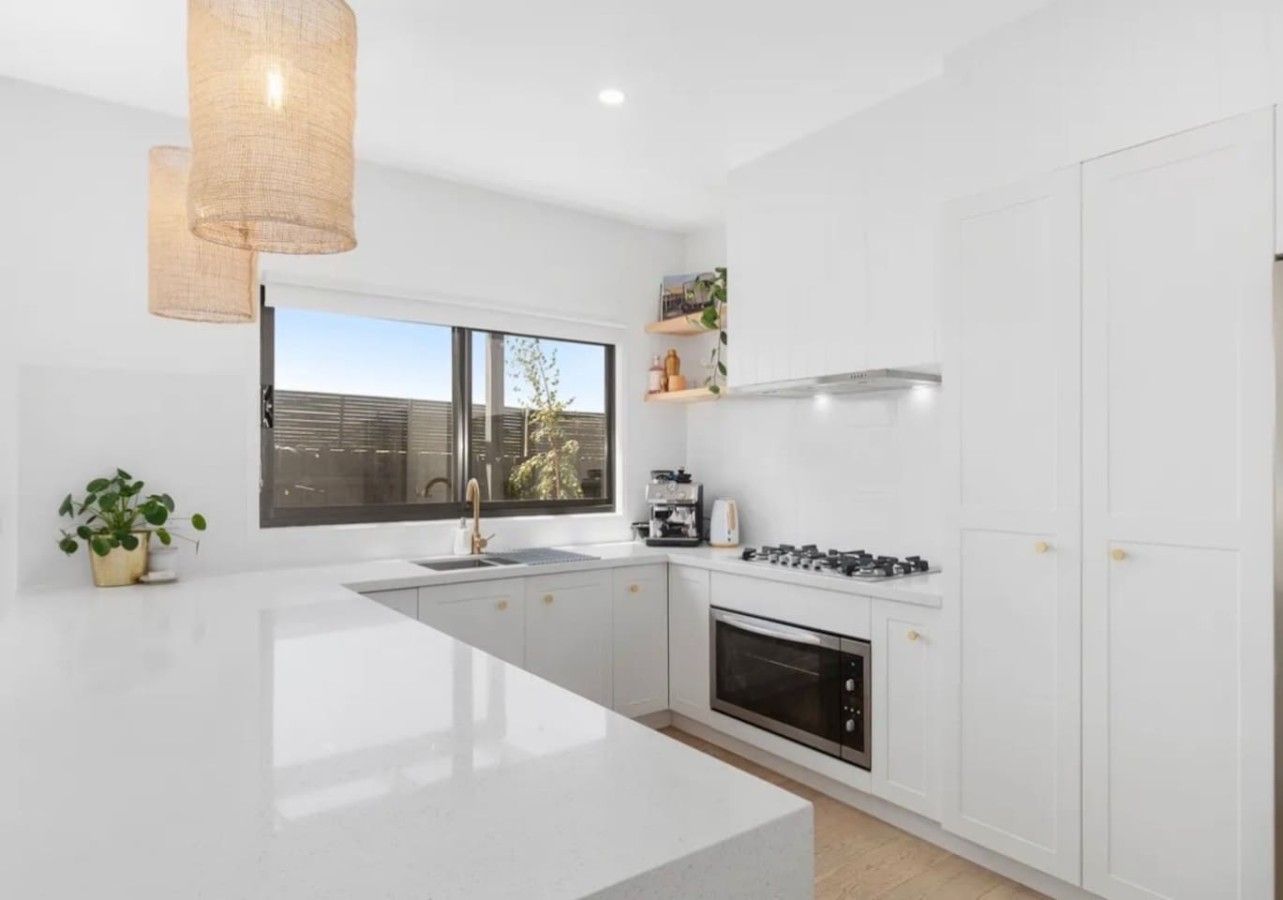 Una cucina moderna con mobili bianchi, un'isola centrale, forno integrato e una finestra che offre luce naturale.