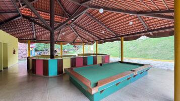 A pool table area with a tiled floor, a wooden table, and a ceiling with a red-tiled roof.