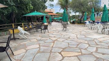 Un patio al aire libre con piso de piedra, mesas, sillas y sombrillas verdes.