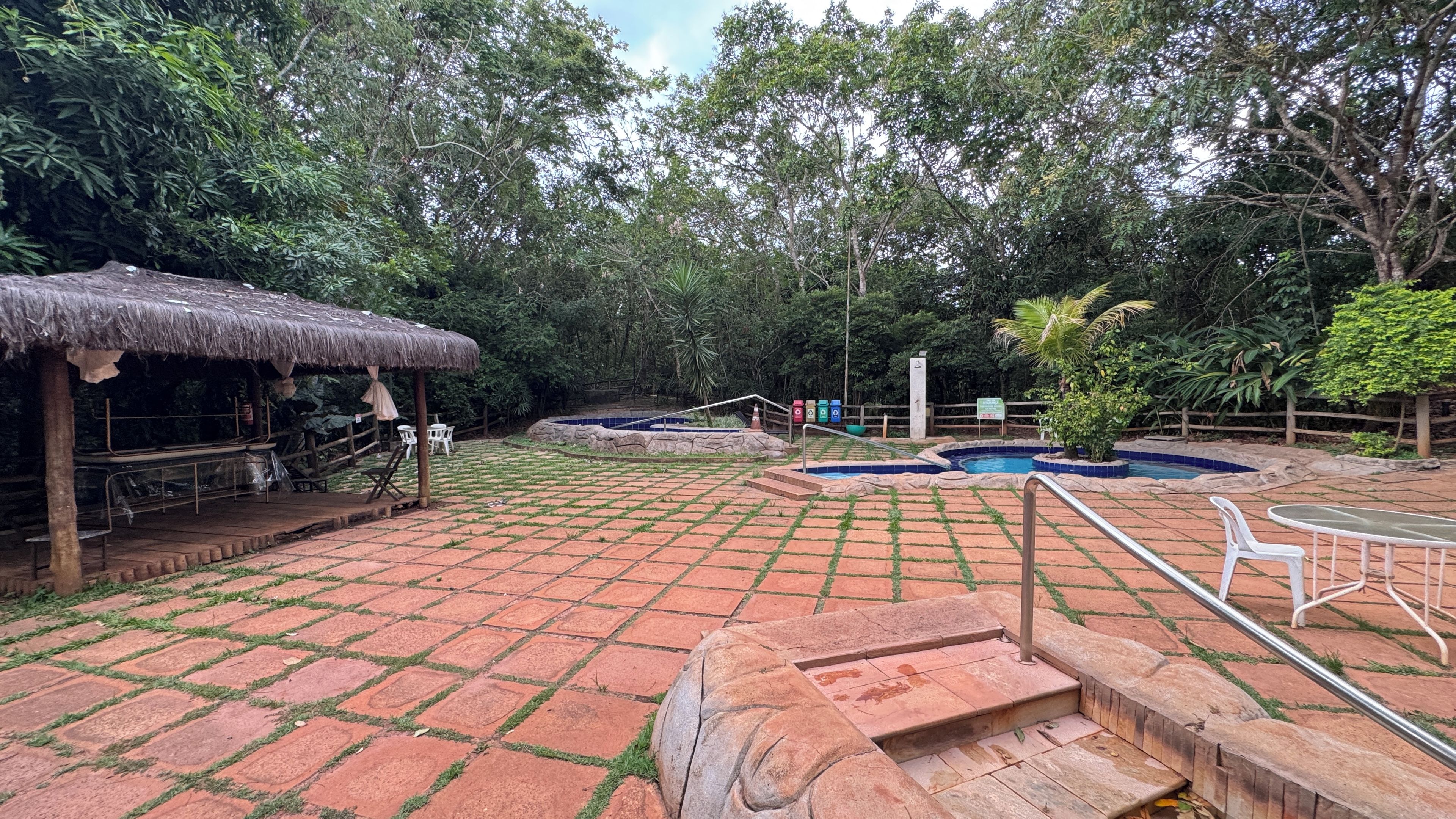 A patio area with a thatched-roof structure, a pool, and a fenced garden.