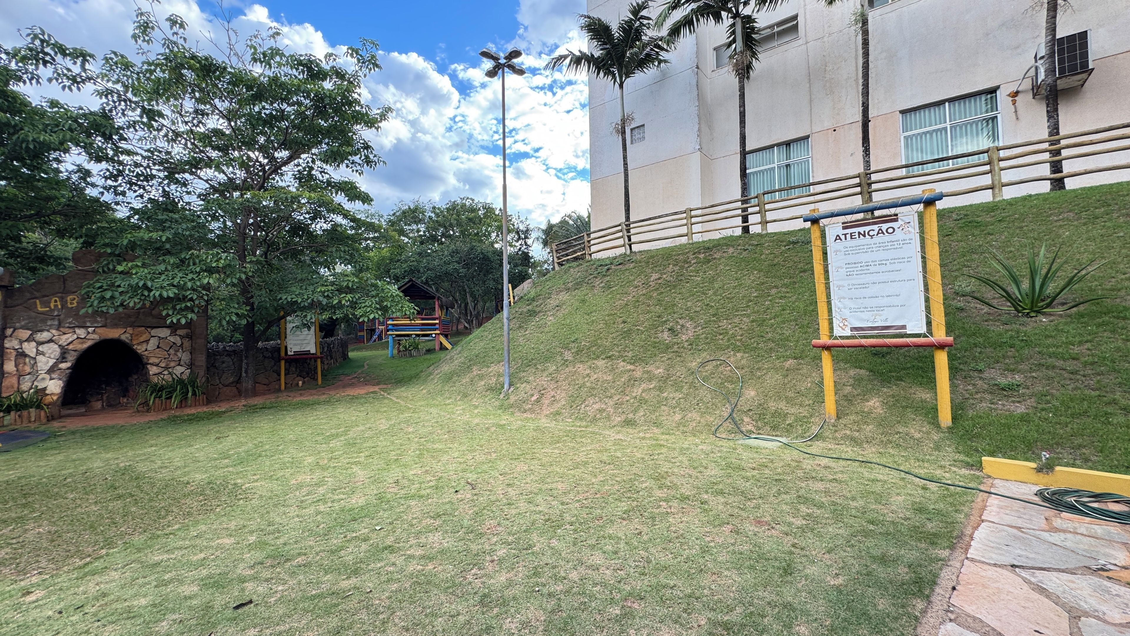 Uma área gramada com um arco de pedra com a inscrição 'LAB', um parquinho e um edifício com uma placa.