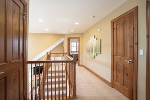 A hallway with wooden doors, a staircase, and a wall with artwork. - Highland Greens Townhome: Long-Stay Lodging, Private Hot Tub (Breckenridge)