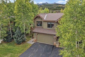 A two-story house with a garage, surrounded by trees and a mountain in the background. - Highland Greens Townhome: Long-Stay Lodging, Private Hot Tub (Breckenridge)