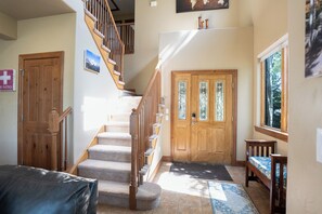 A staircase leading to a second floor, a wooden door with glass panels, a bed with a patterned bedspread, and a window with a view of trees. - Highland Greens Townhome: Long-Stay Lodging, Private Hot Tub (Breckenridge)