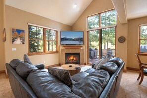 A living room with a leather sofa, a fireplace, a television, and large windows. - Highland Greens Townhome: Long-Stay Lodging, Private Hot Tub (Breckenridge)