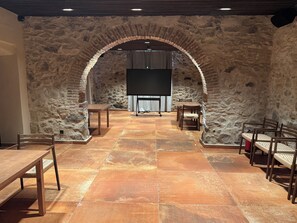 A room with stone walls, a large screen, and a dining area with chairs and tables. - Can Roig Farmhouse (Riells i Viabrea)