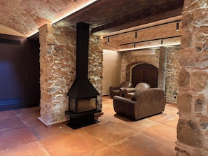 A stone-walled room with a fireplace, leather chairs, and a tiled floor. - Can Roig Farmhouse (Riells i Viabrea)