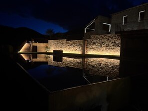 A nighttime view of a building with stone walls and a lit pathway leading to a door. - Can Roig Farmhouse (Riells i Viabrea)