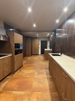 A modern kitchen with wooden cabinetry, a central island, and a built-in oven. - Can Roig Farmhouse (Riells i Viabrea)