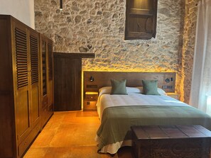 A bedroom with a stone wall, wooden wardrobe, a bed with green pillows, and a nightstand. - Can Roig Farmhouse (Riells i Viabrea)
