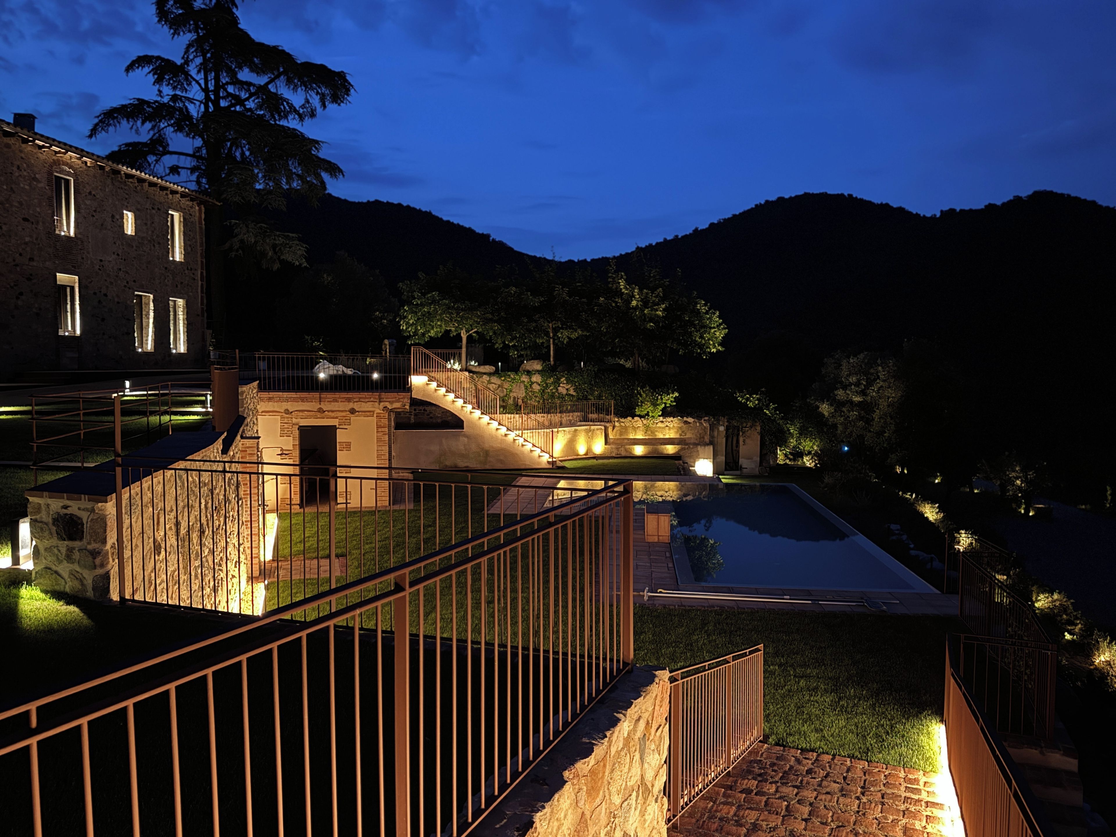 A nighttime view of a building with a swimming pool, a staircase, and a stone wall.