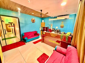 A hotel reception area with a reception desk, a red sofa, and a blue sofa.