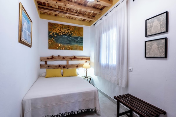 A bedroom with a wooden headboard, a bed with a white bedspread, a bench, and artwork on the walls.