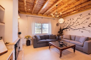 A modern living room with a wooden ceiling, a large window, a sofa, a coffee table, and a wall mural.