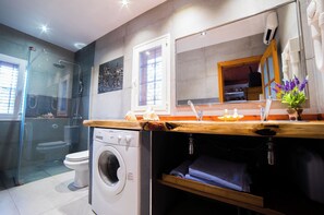 Ein modernes Badezimmer mit einer Duschkabine aus Glas, einer integrierten Waschmaschine und einem Holzwaschtisch mit Spiegel.