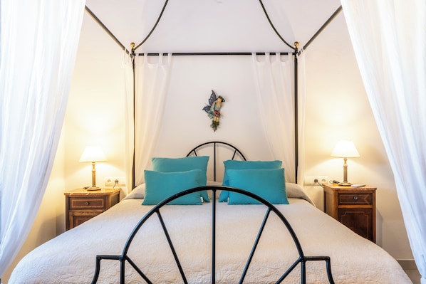 A four-poster bed with a canopy, two bedside tables with lamps, and a decorative wall piece.