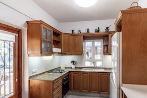 A kitchen with wooden cabinets, a gas stove, a sink, and a window with a view of the outdoors.