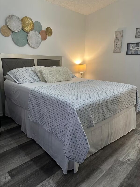 A bed with a patterned bedspread, a headboard, and a bedside lamp.