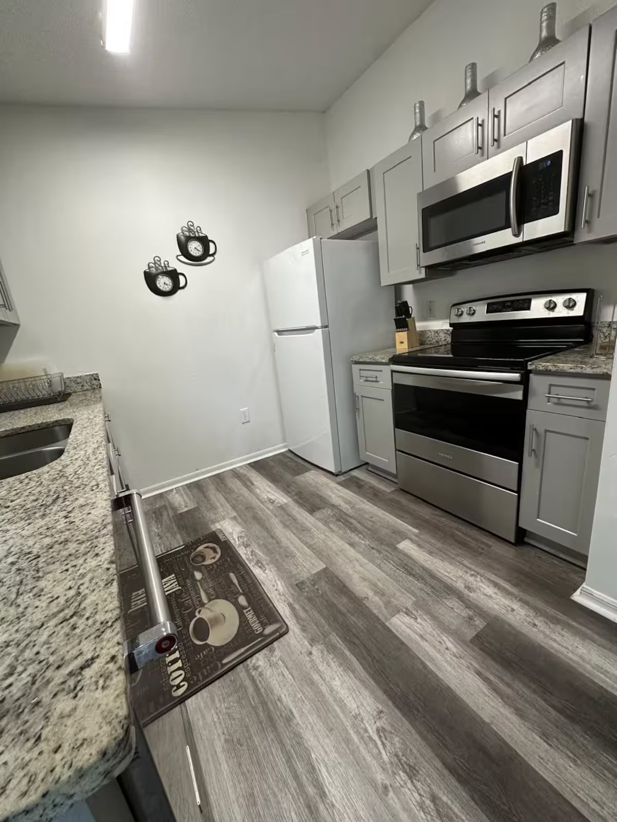 A modern kitchen with stainless steel appliances, a granite countertop, and a wooden floor.