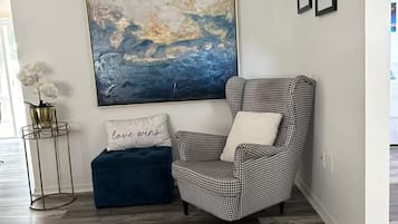 Ein Eckzimmer mit einem Hounds-Tooth-Sessel, einem blauen Hocker und einem großen abstrakten Gemälde.