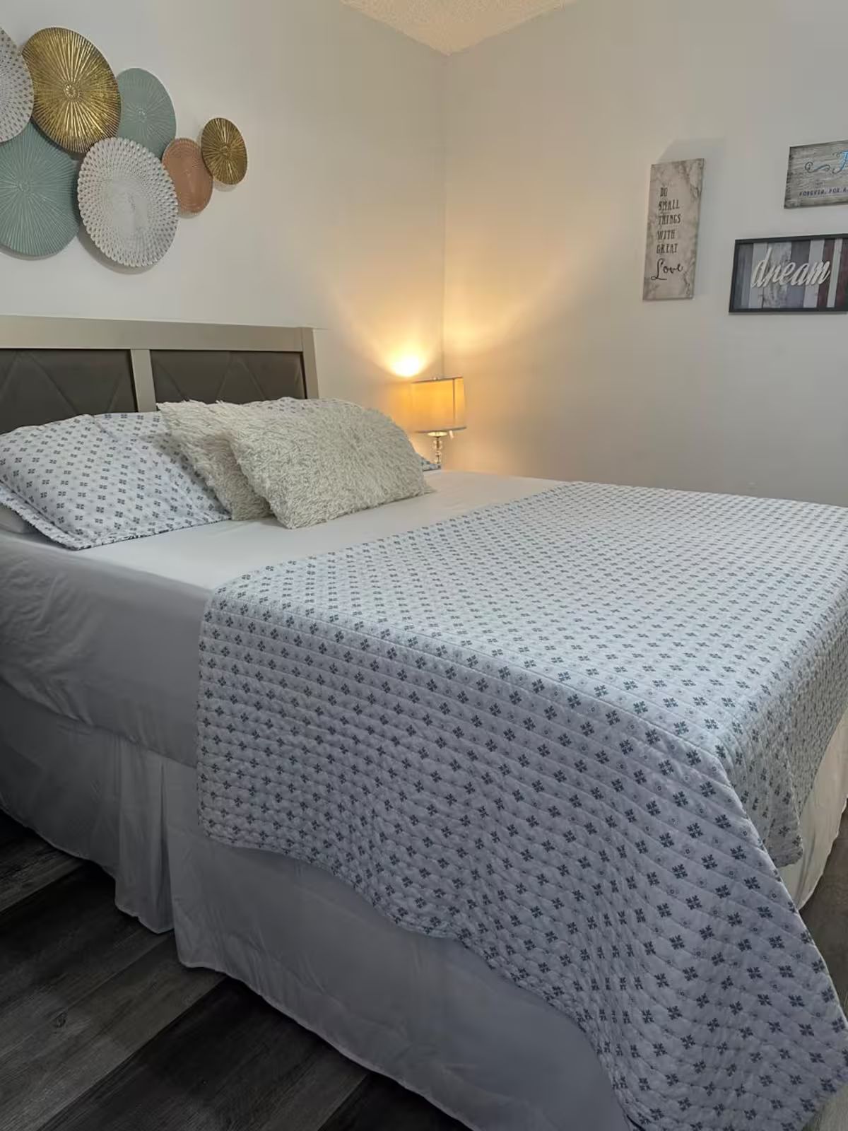 A neatly made bed with a patterned bedspread and pillows, a bedside lamp, and decorative wall art.