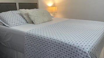 A neatly made bed with a patterned bedspread and pillows, a bedside lamp, and decorative wall art.